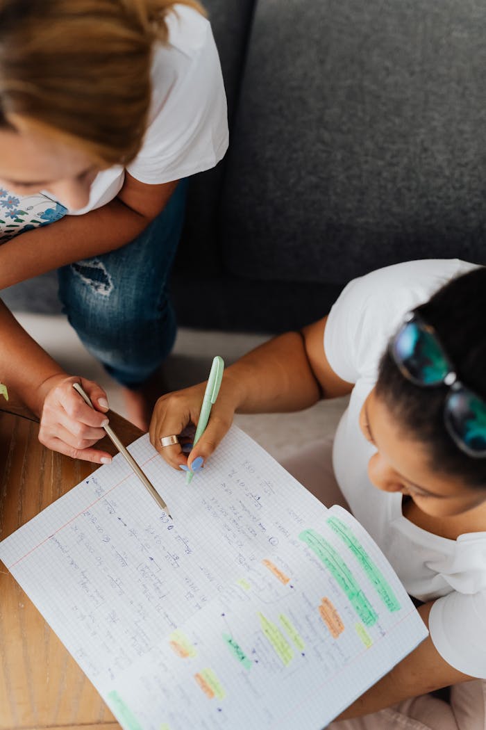Two women collaborating on a study session with notes and pens, viewed from above.