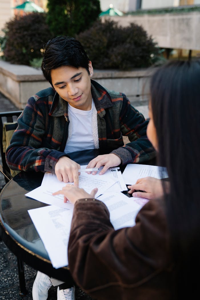 Two young adults studying together at an outdoor table, collaborating on a project.